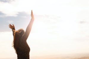 woman with arms raised standing in sunlight