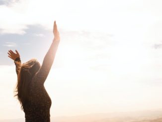 woman with arms raised standing in sunlight